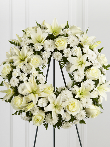 White floral standing wreath with roses, lilies and greenery displayed on an easel