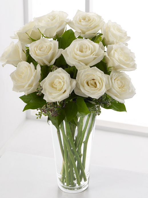 Twelve white roses with greenery arranged in a clear glass vase