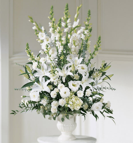 Tall white sympathy arrangement with lilies, gladiolus and snapdragons in a classic container