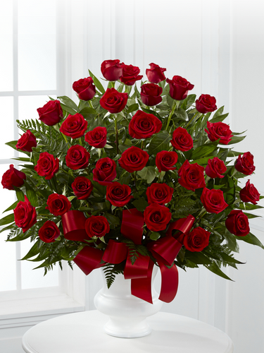 Thirty-six red roses with greenery and red ribbon arranged in a white pedestal container