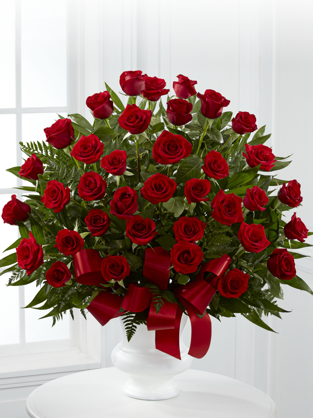 Thirty-six red roses with greenery and red ribbon arranged in a white pedestal container
