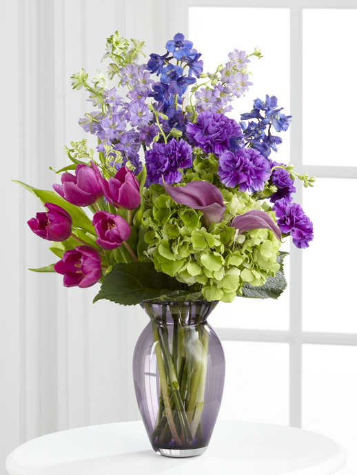 Lavender and blue sympathy flowers with tulips, delphinium, calla lilies and hydrangea in a glass vase