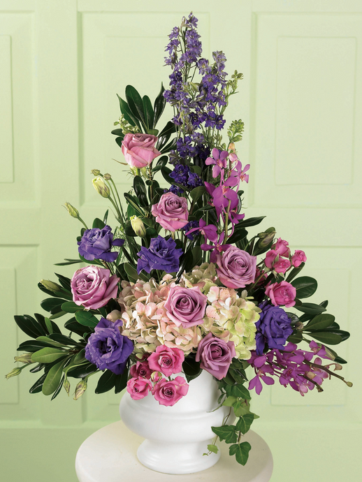 Lavender and pink floral arrangement with roses, hydrangea and greenery in a white pedestal container
