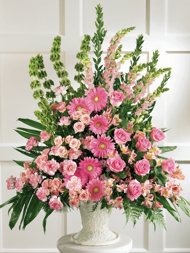 Large pink floral arrangement with roses, gerbera daisies and greenery in a white pedestal container