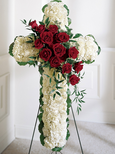 Standing floral cross of white carnations with cascading red roses and greenery