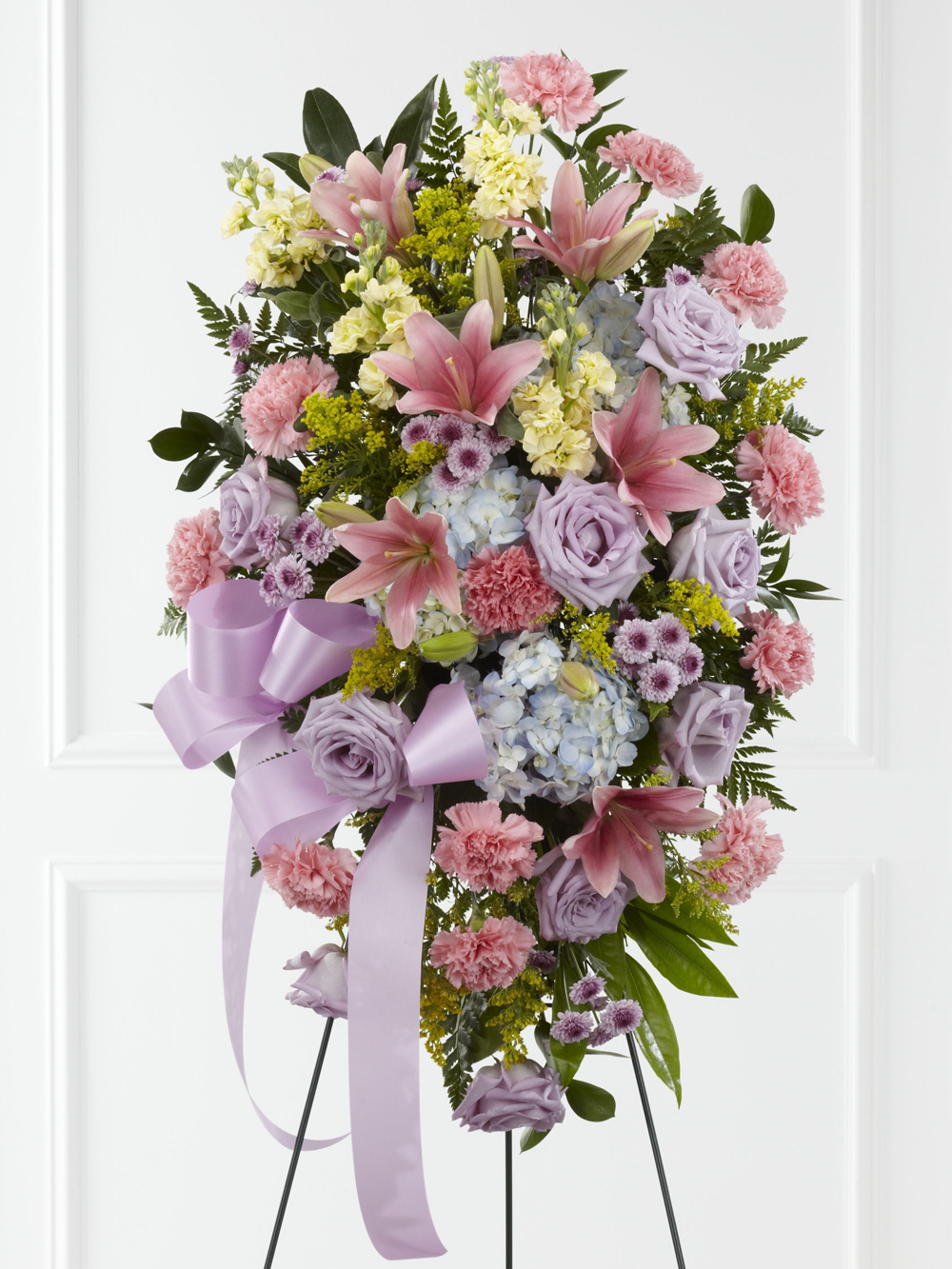 Pastel standing spray with pink lilies, lavender roses, carnations and blue hydrangea on an easel